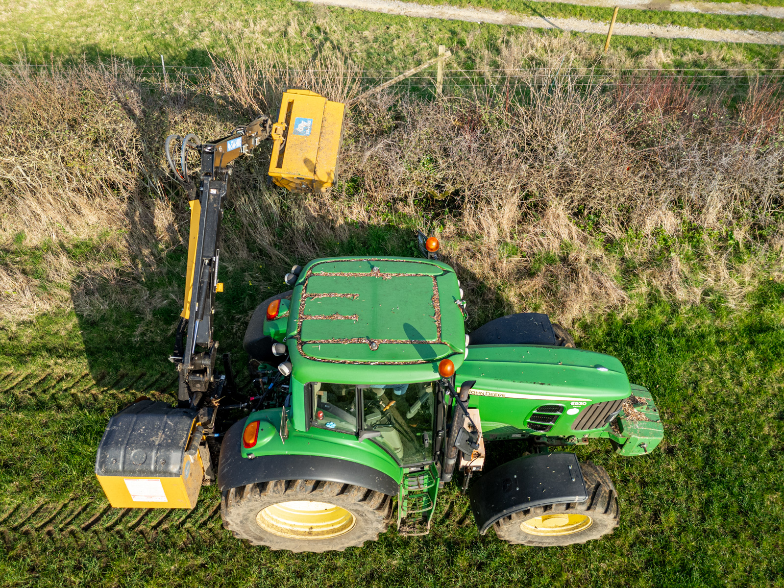 McConnel P6567T power arm mounted on a John Deere tractor cutting a hedge in a grass field